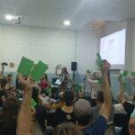 Persones aixequen cartolines verdes amb la mà per votar a l'assemblea d'una cooperativa.